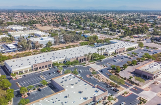An aerial color photograph of a large industrial building and parking lot surrounded by street trees and other buildings.